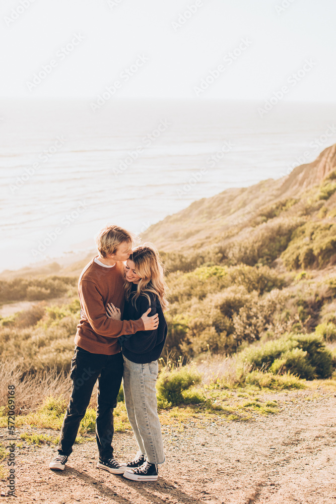 couple embracing with the man kissing the woman on the cheek standing by the cliff over the ocean