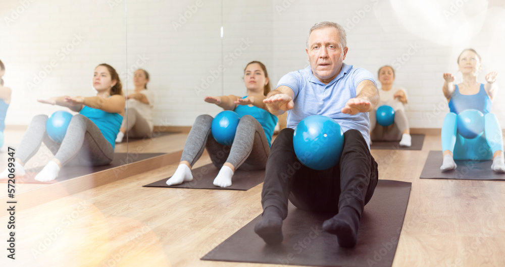 Obraz premium Willing aged man engaging in pilates training with ball in gym room during workout session. Persons practicing pilates in fitness studio