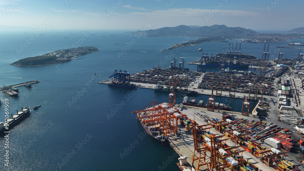 Aerial drone photo of huge fully loaded container tanker ship reaching with help of tug boat logistics and container terminal of Perama, Attica, Greece