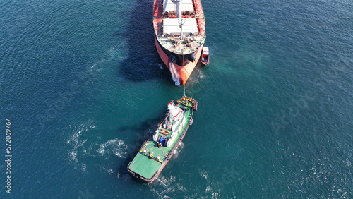 Aerial drone top down photo of super tanker towed by tug boat in deep blue sea near logistics container terminal port © aerial-drone