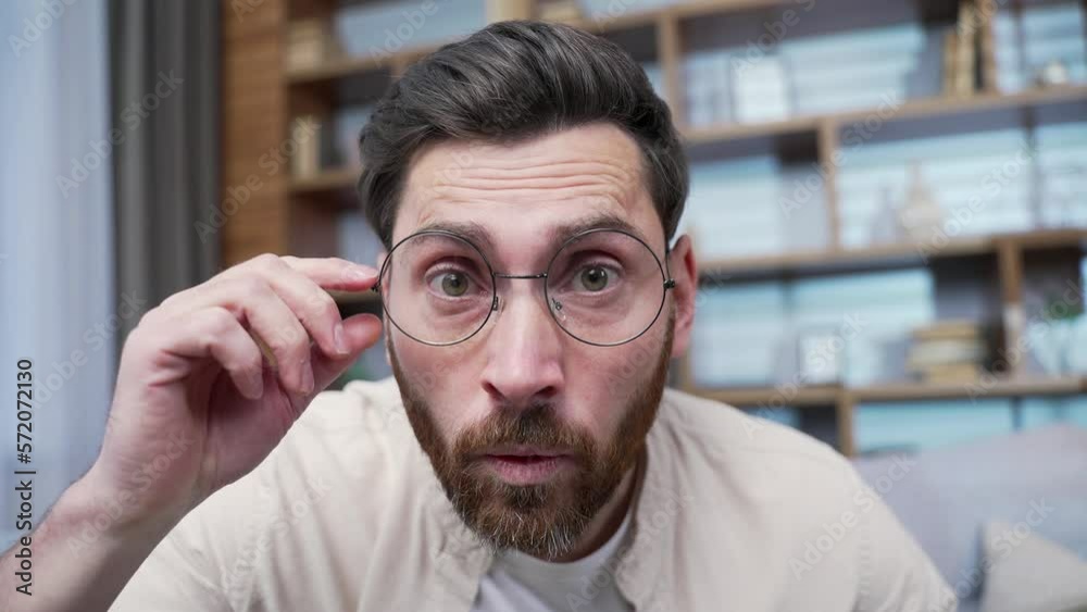 Camera view of amazed shocked bearded man with glasses staring into camera demonstrates wow surprised face expression indoors Happy male rejoices by sudden incredible news promotion sale at home 