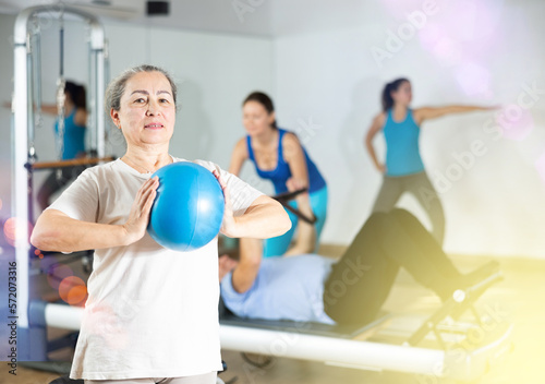 Smiling old female pensioner squeezing ball in hands during Pilates training in rehabilitation center