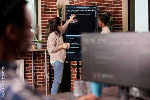 Team of coders talking about algorithms in front of big screen, analyzing html script language. Software developers discussing database on terminal window working in it programming agency photo