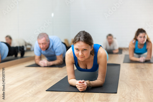 People of different ages in sportswear performing plank exercise during group Pilates workout in fitness studio