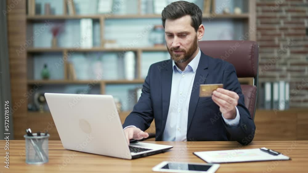 Smiling business man entrepreneur paying with credit card on laptop computer at the office workplace Happy customer employer do payments online shopping in internet store and receive cashback Easy pay Smiling business man entrepreneur paying with credit card on laptop computer at the office workplace Happy customer employer do payments online shopping in internet store and receive cashback Easy pay
