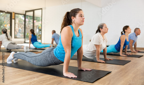 Slim sporty young girl practicing pilates during group training in fitness center, performing back bending exercise