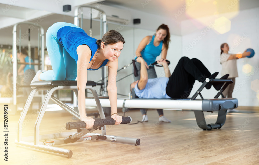 Fototapeta premium Positive middle-aged woman performing stretching exercises while using pilates Wanda chair machine in rehabilitation center