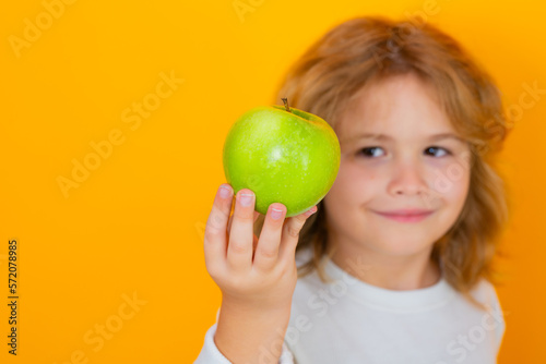Kid with apple in studio. Studio portrait of cute child hold apple isolated on yellow background.