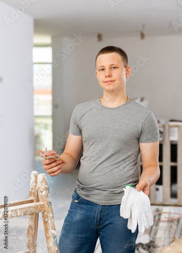 Satisfied fifteen-year-old teenage boy working on a construction site indoors during renovation work in a home, holds the ..first salary in his hands photo