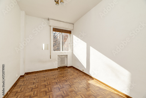 Empty room with wood-look sintasol flooring, iron radiator in a niche and interior window with shutters and view