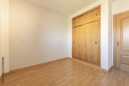 Empty room with a built-in wardrobe with light wood sliding doors and floating wood flooring