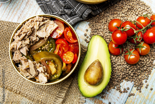 A wonderful canned tuna salad with diced tomatoes and avocados in a golden bowl with pepita tomatoes and avocado over dried lentils