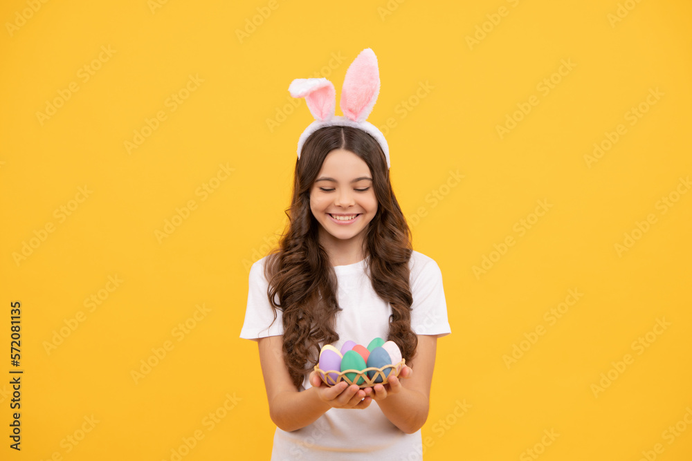 happy child in bunny ears hold eggs on yellow background, easter