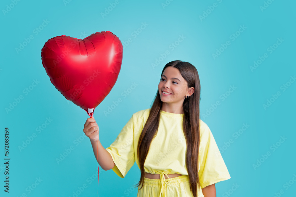 Teenager child girl with love romantic gift, sweetheart. Valentines sale. Portrait of child with heart balloon isolated on blue studio background. Happy girl face, positive and smiling emotions. Teenager child girl with love romantic gift, sweetheart. Valentines sale. Portrait of child with heart balloon isolated on blue studio background. Happy girl face, positive and smiling emotions.