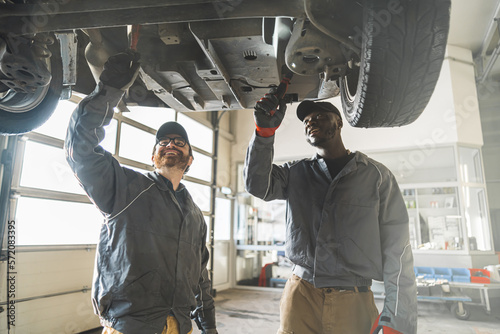 two servicemen working on a car using special tools, medium shot car workshop. High quality photo © PoppyPix