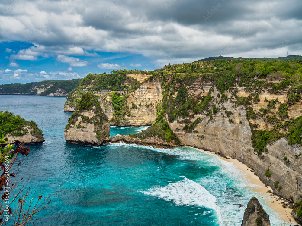 Atuh Beach is a Rustic, isolated cove beneath a sheer cliff face, with a sandy beach offshore rock formations.