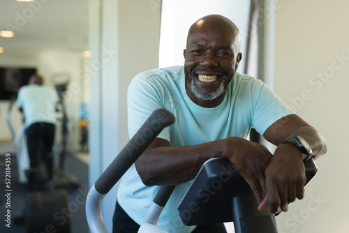 Portrait of african american senior man smiling while standing on elliptical machine at the gym photo