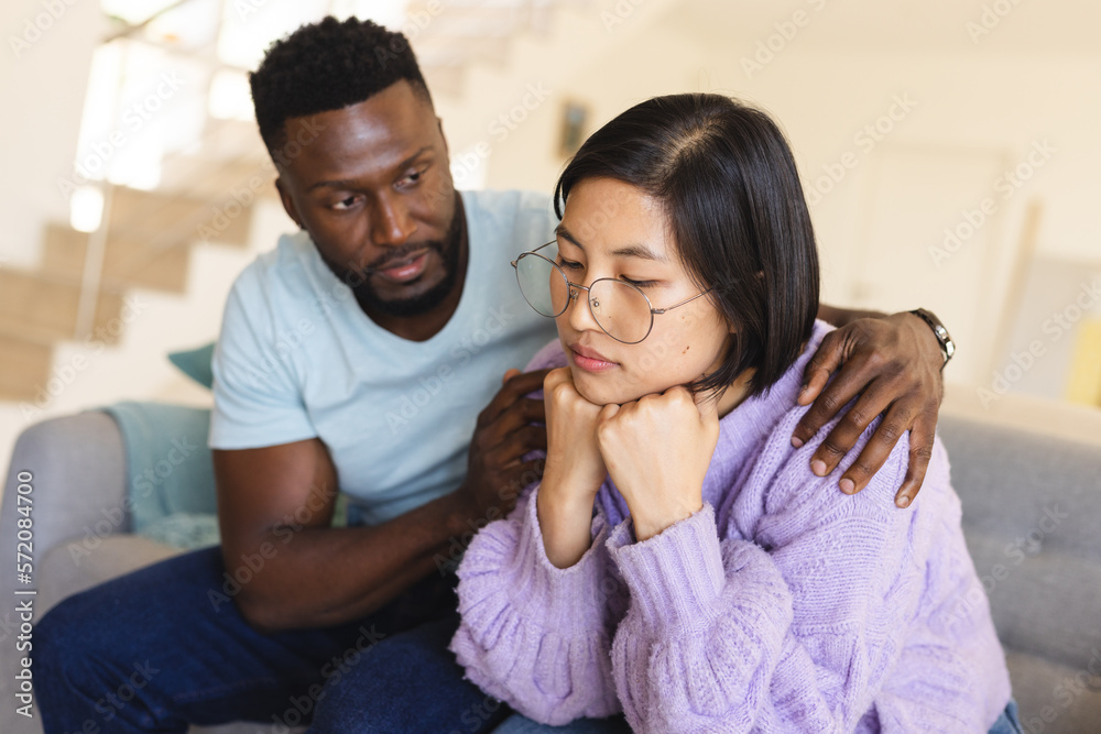 Sad diverse couple sitting on sofa and embracing