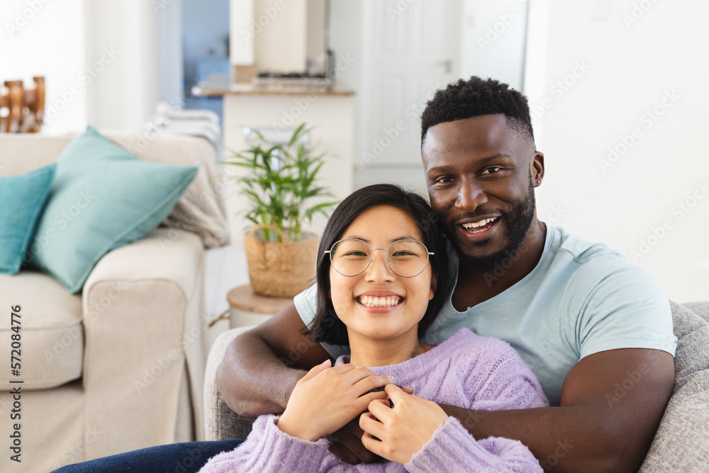 Portrait of happy diverse couple sitting on sofa and embracing Portrait of happy diverse couple sitting on sofa and embracing