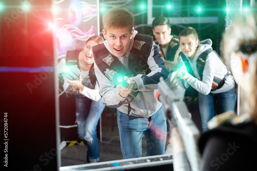 Happy teen boy with laser pistol playing laser tag with friends on dark labyrinth..