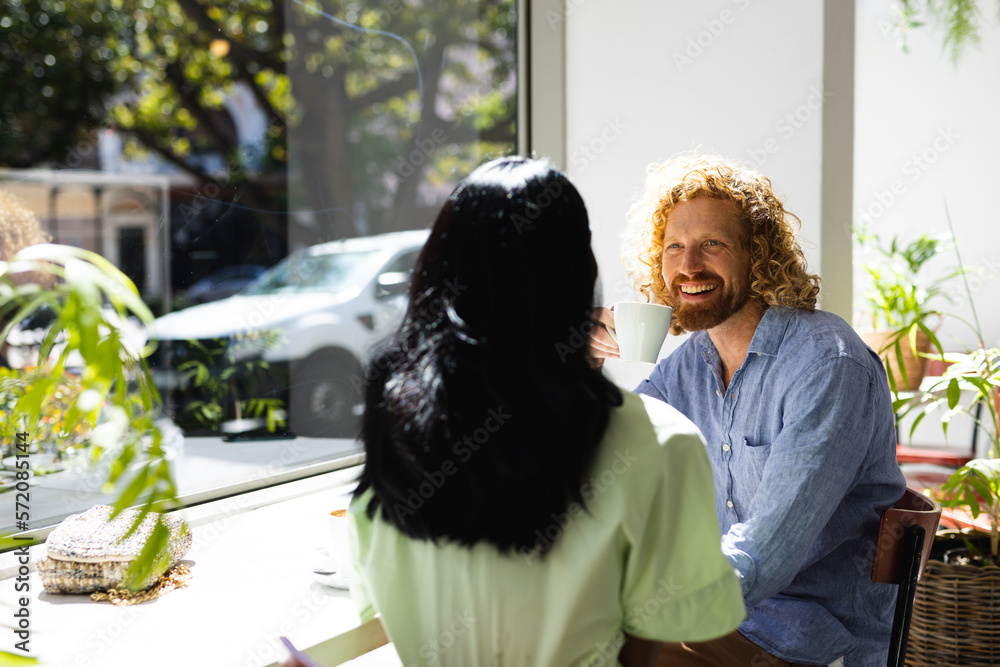 Happy diverse couple sitting at table and talking with cup of coffee in cafe Happy diverse couple sitting at table and talking with cup of coffee in cafe
