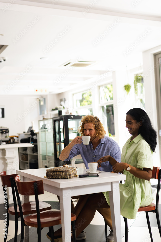 Happy diverse couple sitting at table and talking with cup of coffee in cafe Happy diverse couple sitting at table and talking with cup of coffee in cafe