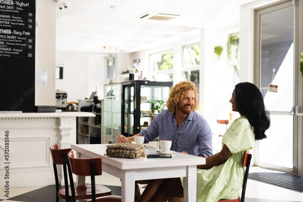 Happy diverse couple sitting at table and talking with cup of coffee in cafe Happy diverse couple sitting at table and talking with cup of coffee in cafe