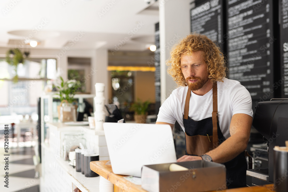 Caucasian male barista wearing apron and using laptop in cafe Caucasian male barista wearing apron and using laptop in cafe