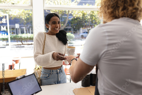 Happy diverse male barista and woman ordering cup of coffee in cafe
