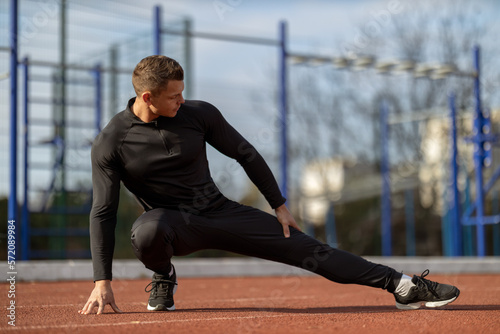 Athletic man in black sportswear stretches his muscles before training