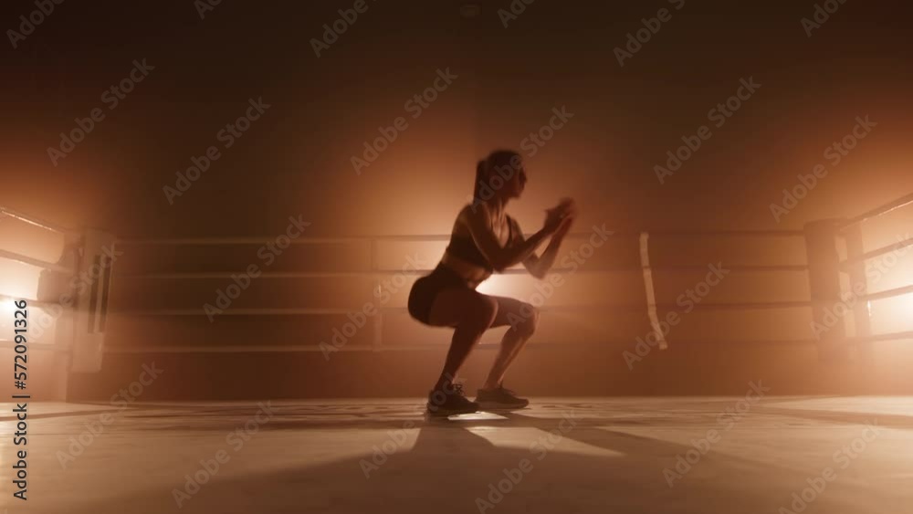 Close-up of a squatting female champion with dramatic light in the background. Silhouette of a woman in sporty shape strengthening her lower body muscles and fitness. High quality 4k footage Close-up of a squatting female champion with dramatic light in the background. Silhouette of a woman in sporty shape strengthening her lower body muscles and fitness. High quality 4k footage