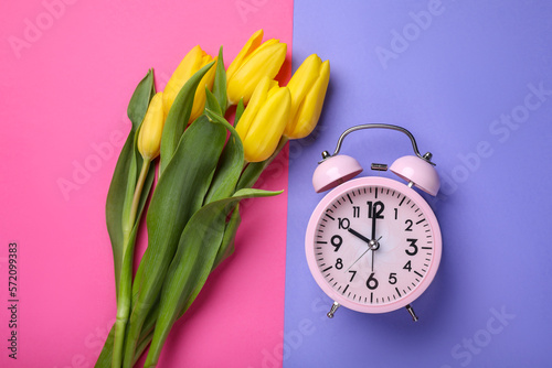 Pink alarm clock and beautiful tulips on color background, flat lay. Spring time