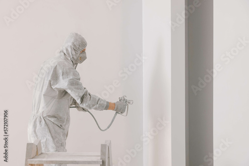 Vászonkép Decorator in uniform painting wall with sprayer indoors