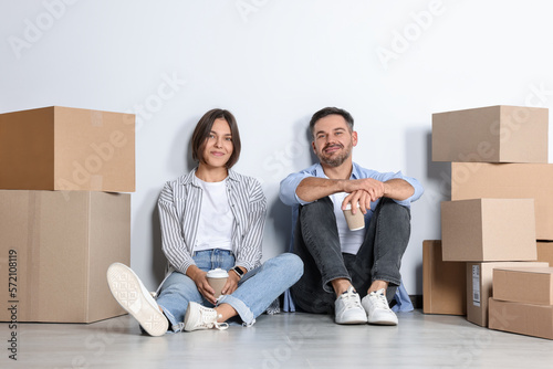 Happy couple with takeaway coffee resting on floor in new apartment. Moving day © New Africa