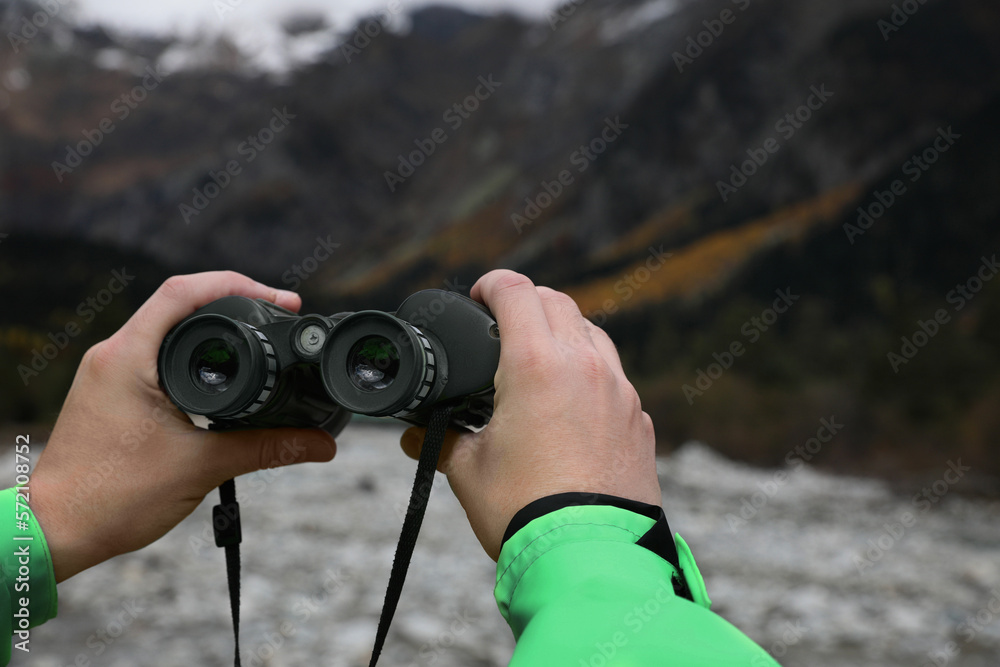 Woman holding binoculars near river in beautiful mountains, closeup. Space for text