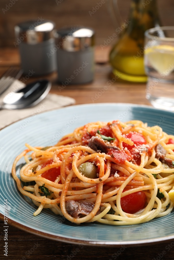 Delicious pasta with anchovies, tomatoes and parmesan cheese served on wooden table, closeup