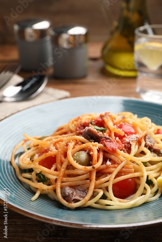 Delicious pasta with anchovies, tomatoes and parmesan cheese served on wooden table, closeup