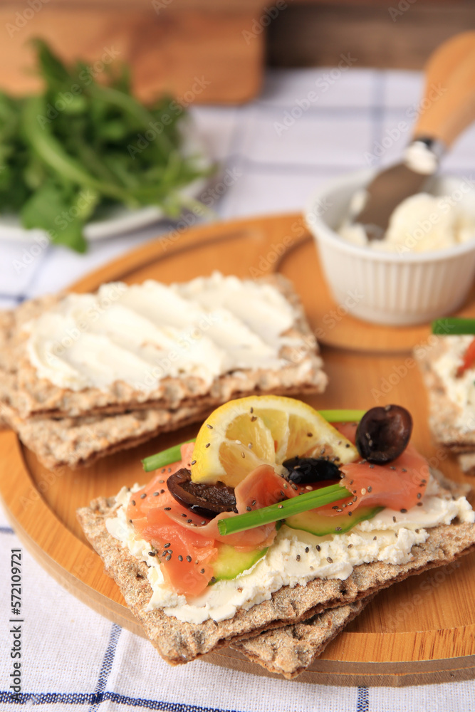Fresh crunchy crispbreads with cream cheese, salmon, olives, lemon and green onion on table, closeup