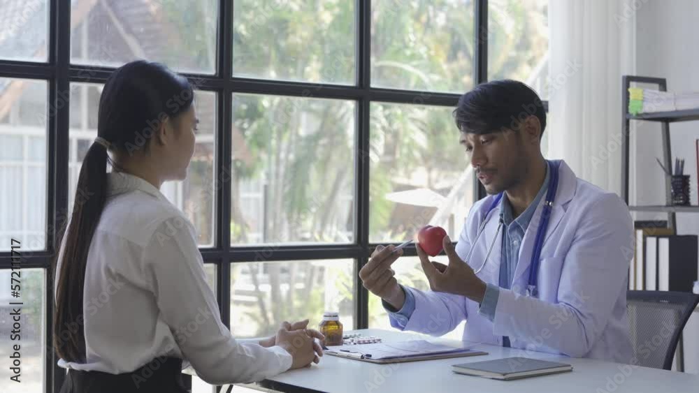 Friendly doctor or Asian male helping discuss medicine and heart disease with medical tests at clinic desk. A young woman with severe stress visits a doctor at the hospital. Friendly doctor or Asian male helping discuss medicine and heart disease with medical tests at clinic desk. A young woman with severe stress visits a doctor at the hospital.