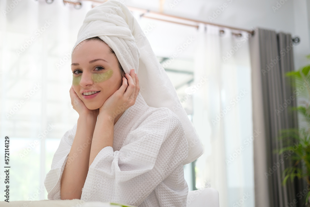 Attractive caucasian woman in bathrobe and towel wrapped on head applying  eye patches for dark circles removal,.