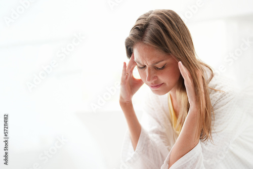 Young Caucasian woman is unwell and appears to be experiencing a migraine headache. She is touching  her head while in a brightly lit room. It appears that she is suffering from a health problem. photo