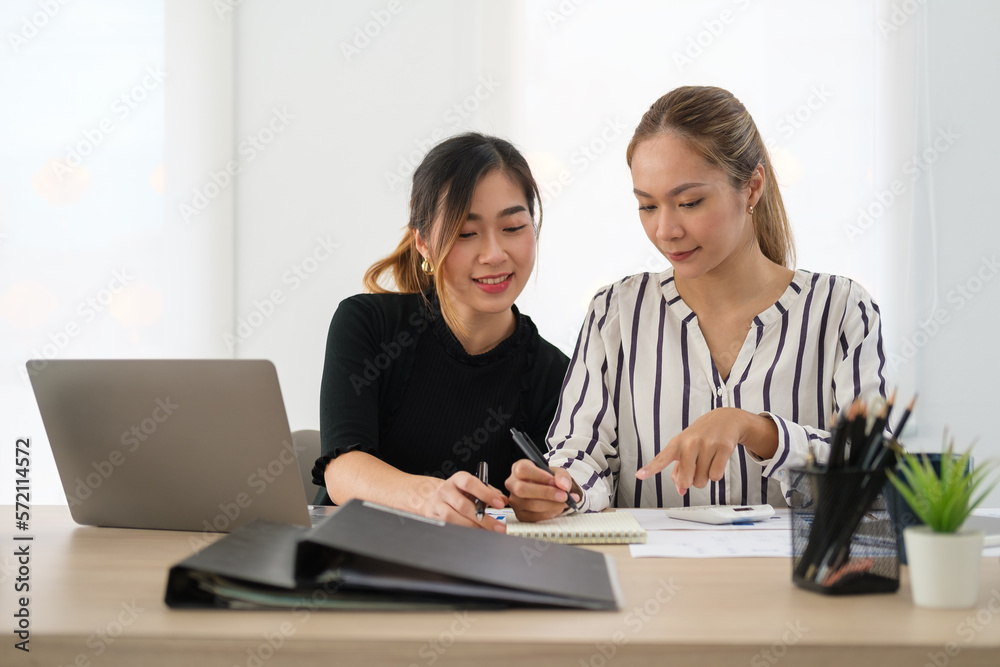 Smiling asian female employee pointing on notepad and explaining new idea to her colleagues. Smiling asian female employee pointing on notepad and explaining new idea to her colleagues.