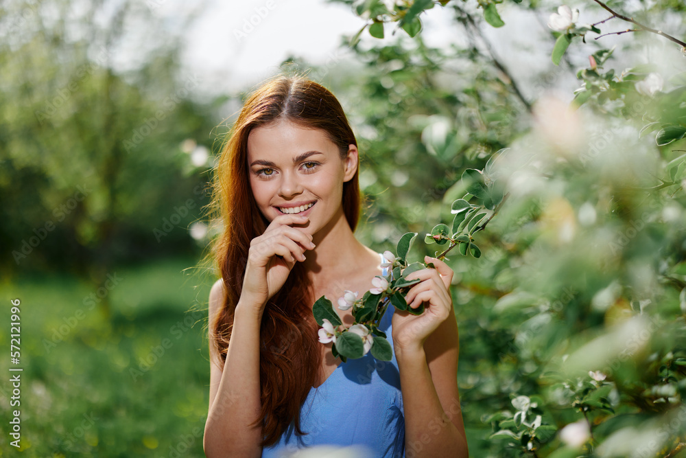Woman portrait beautifully smiling with teeth spring happiness in nature against a green tree tenderness hand touching a branch of a blooming tree, safety from allergies and insects
