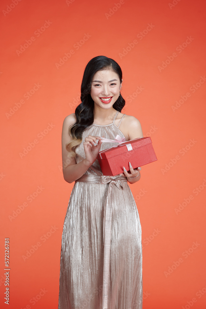 Portrait of an excited cute girl in dress holding opened present box isolated over red background Portrait of an excited cute girl in dress holding opened present box isolated over red background