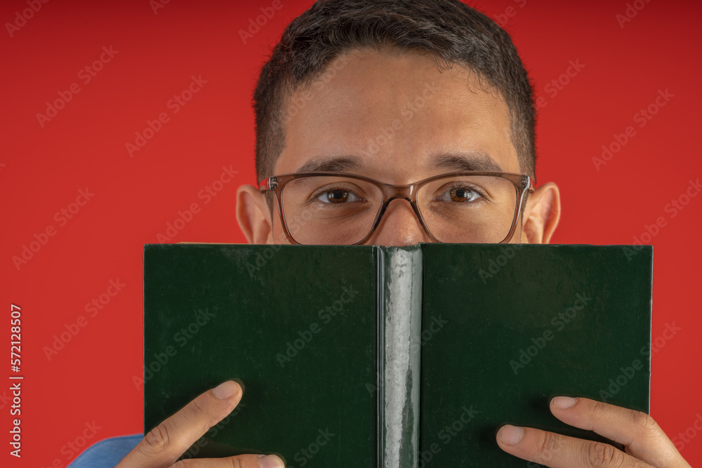 Young man with glasses holding a hardcover book in front of his face Young man with glasses holding a hardcover book in front of his face