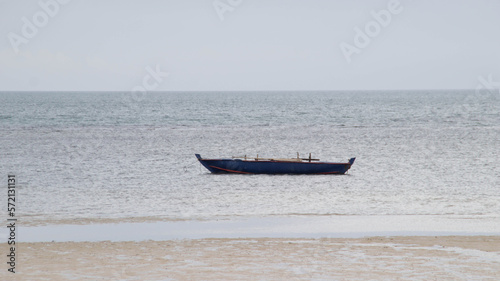 Small short blue wooden boat for fishing and transporting tied up at the shallow sea.
