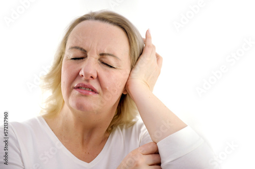 headache middle-aged adult woman interferes with noise she closes her ears squinting her eyes bent over with a displeased face hurts head pain in the ear white background white jacket unpleasant photo