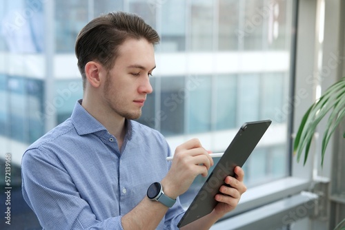 Young man, office worker or student is using tablet computer, device with electronic pen or pencil, drawing or writing 