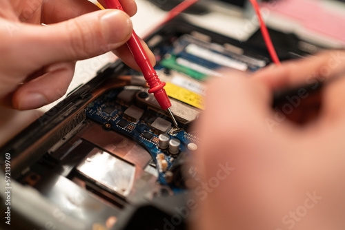 Close up of male hands testing laptop motherboard using multimeter.