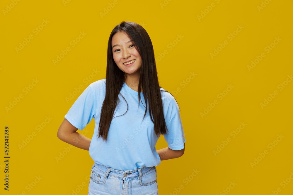 Asian woman smile with teeth hand gestures, signs and symbols on yellow background in blue t-shirt and jeans Asian woman smile with teeth hand gestures, signs and symbols on yellow background in blue t-shirt and jeans